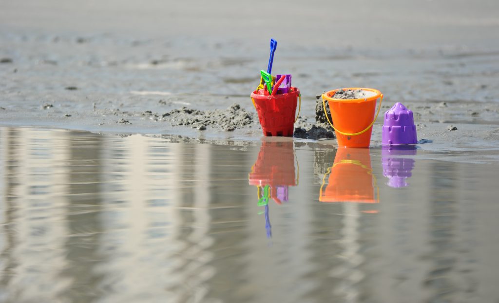 beach pails red, orange and purple with shovels on sand and water