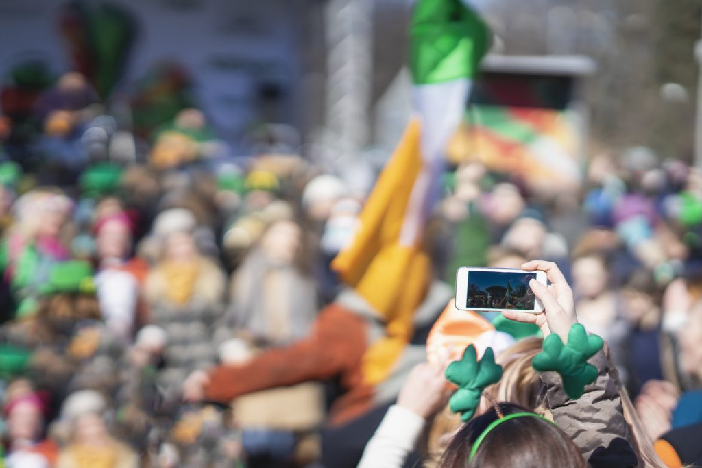 Hands of girl with mobile phone, making photo, video of carnival of St. Patrick's Day, traditional carnival party on a smartphone