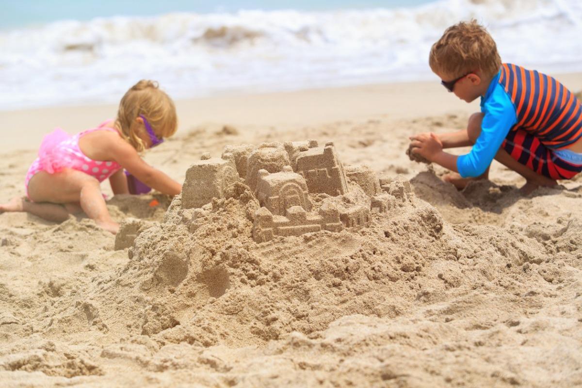 little boy and girl building sand castle on summer beach with waves in the background